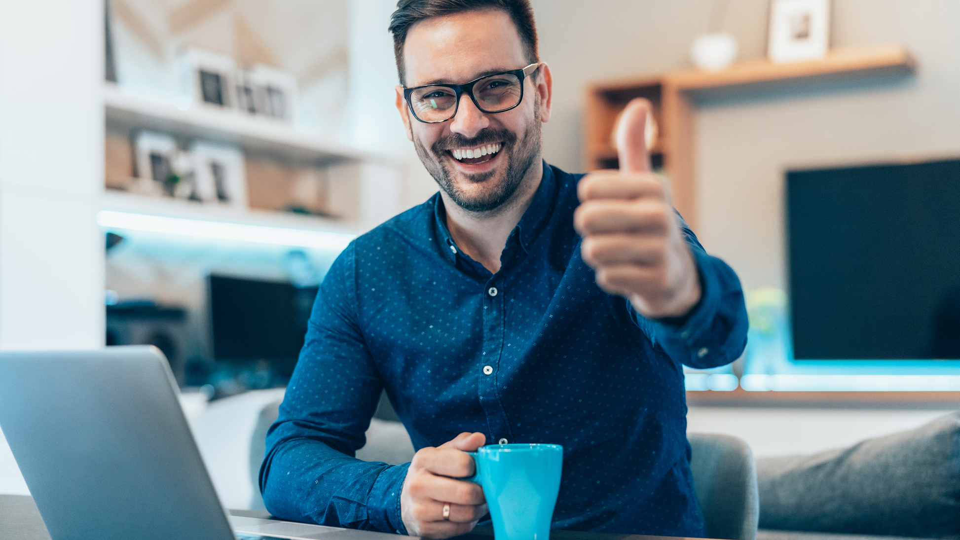 an image of smiling male, holding a cup of coffee, wearing reading glasses and guy showing thumbs up in front of a laptop
